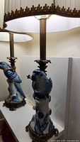 Close-up of one porcelain parrot lamp base showing the detailed blue and white hand painted porcelain bird, brass fittings, and lamp stem with fabric shade above