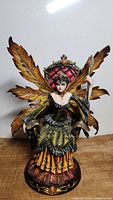 Front view of Fairy figurine showing detailed autumn leaf wings, multi-colored layered dress, and seated pose on throne.