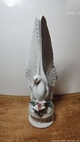 Front view of white dove figurine with wings raised, showing detailed feathers and base with pink bow and fruit accents.