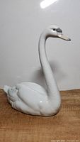 Front and side views of white porcelain swan figurine showing elegant long curved neck, detailed wings, and painted natural colored beak and grey eyes.