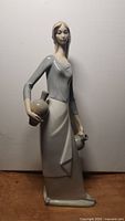 Side profile view of the figurine showing the lady holding two jugs, highlighting the delicate features and glazing.