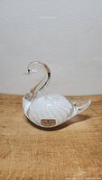 Side view of Marcolin crystal swan figurine on wooden surface against a plain wall background.