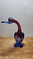 Front left angle showing the full figure of the glass goose with blue feet and beak, red neck and blue body.