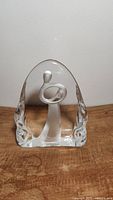 Clear and frosted glass figurine of mother holding baby on wood surface, front view