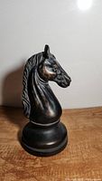Side view of the black horse head chess piece statuette showing detailed mane and facial features on wooden surface.