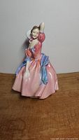 Front view of the porcelain figurine showing the lady in a pink dress with a blue-green sash and white ruff.
