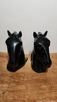 Front view of two glossy black horse head bookends on a wooden surface against white background