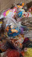 Box filled with various McDonald's Happy Meal toys in original sealed bags, showing colorful plastic figures and packaging with McDonald's branding and numbering.