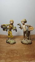 Front view of two resin figurines, one boy holding grapes and the other with fish and lobster
