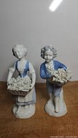 Pair of Gerold Porzellan Bavaria porcelain figurines, girl and boy holding trays of flowers, displayed on wood surface with bright lighting.