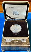Coin displayed inside official velvet-lined presentation box with lid open, showing informational insert.