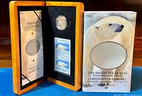 Wooden display case open showing the certificate of authenticity on the left panel and inside right panel with a silver coin above two 2-dollar Canadian polar bear stamps.