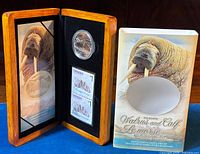 Wooden display case holding the coin and stamps with original outer sleeve showing Atlantic Walrus image.
