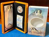 Wooden display case open showing coin and two stamps inside next to protective card sleeve with falcon images