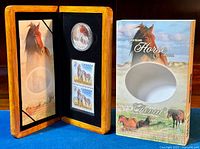 Open wooden display case with encapsulated $5 coin and two $2 stamps inside along with partially visible booklet.