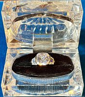 Ring with cushion-cut clear CZ set in sterling silver shown inside an open clear display box with black velvet interior.