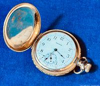 Opened hunter case showing white porcelain dial with cracks and Waltham branding, dial numbered with Arabic numerals and subdial for seconds.