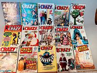 Photo showing 16 CRAZY magazine issues laid out in 3 rows with colorful and varied covers including Santa, UFO themes, caricatures, and comic-style illustrations.