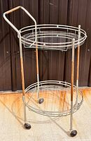 Full view of bar cart showing metal frame, wooden handle and leg accents, glass shelves, and caster wheels.