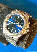 Close-up of Seiko Kinetic Sports men's watch showing blue dial with Seiko Kinetic branding, day/date window, and stainless steel casing and bracelet.