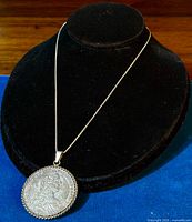 Full view of sterling silver box chain necklace with coin pendant displayed on black velvet stand.