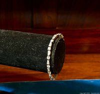 Designer 925 sterling silver tennis bracelet shown elegantly displayed on a black velvet bracelet stand against a wood background.