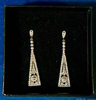 Photo showing a pair of long triangle drop earrings in black velvet display box.