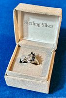 Close-up photo of the ring in its box showing the marquise design with blue and clear stones.