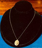 Full view of gold-filled oval pendant on vintage chain displayed on black stand.