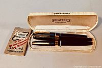 Original set with two Shaeffer's pens (one black, one blue) and manual in an open cream box showing satin lining and Shaeffer's logo.