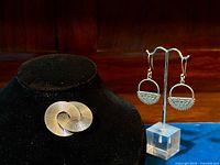 Brooch displayed on black stand beside earrings on clear stand showing overall items in the lot.