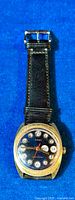 Front view of vintage Timex watch with black dial, gold-plated case, and black leather strap on blue background.