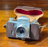 Front view of vintage Miranda film camera in brown leather case, showing metallic lens and camera body details.