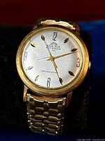 Close-up of vintage Solar wristwatch dial showing brand name, self-winding and shock resistant text, gold tone case and scuffed crystal.