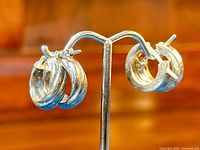 Close-up photo of two vintage sterling silver small hoop earrings displayed on a metal stand against a wood background showing their round shape and post backs.