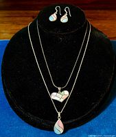 Photo shows the set of mother of pearl inlaid sterling silver earrings and two pendants displayed on black velvet stand with blue cloth background.