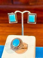 Close-up of sterling silver earrings with square turquoise stones mounted and ring with oval turquoise stone against a wood background.