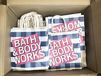 Small Bath & Body Works paper bags with a blue and white checkered pattern and pink logo, stacked showing handles.