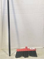 Photo showing long black broom handle vertically positioned against wall, threaded end visible.
