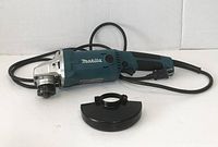 Side view of Makita GA5010 angle grinder with power cord and a black protective guard placed in front.