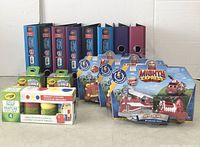 Image shows 8 Avery binders organized standing upright, 2 boxes of Crayola chalk, 2 Mighty Express Rescue Train toys in packaging, and 2 small paint sets in front.