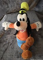 Front view of Goofy plush toy with outstretched arms wearing orange shirt and blue pants and signature green hat