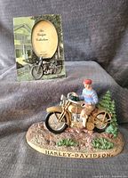 Ceramic Harley Davidson motorcycle doorstop with rider and scenery base with picture frame in the background.