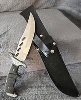 Knife with silver blade featuring cutouts and decorative handle positioned out of sheath.