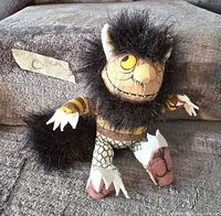 Plush doll with black fur, claws, yellow eyes, and stitched face, sitting on a carpeted surface.