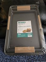 Stack of three new InStyle cookie sheets sealed in plastic with product label showing details.