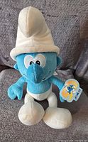 Front view of the blue Smurf plush with white hat and pants, with attached tag showing Smurf logo.