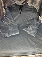 Photo showing full front view of dark grey men's long sleeve 1/4 zip pullover laid flat, displaying front zipper and logos.