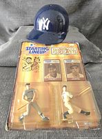 Photo of Mickey Mantle and Joe DiMaggio Starting Lineup Baseball Greats figures in original packaging with a used New York Yankees batting helmet on top.