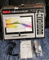 Original RCA 22 inch Full HD LCD TV box showing product features including 1080p resolution, HDMI input, 16:9 aspect ratio, 1920x1080 resolution, 1000:1 contrast ratio, 300 cd/m2 brightness, and 5ms response time. Accessories laid out include remote control, power cord, and user manual.